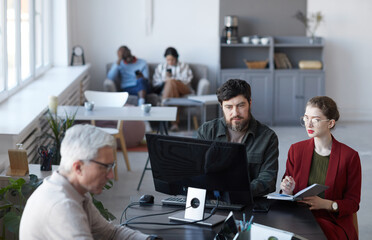 Obraz premium High angle portrait of bearded business manager talking to female colleague during meeting at table in white office interior