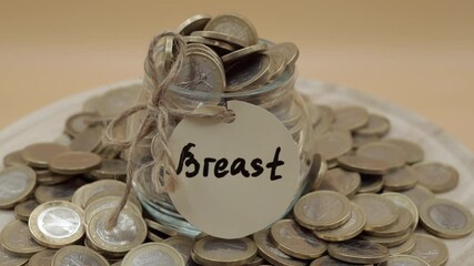 Stack of coins on isolated orange background, glass jar with breast inscription rotating. Budget planning and earnings investments in body procedures of beauty industry, strategy of saving and making - Powered by Adobe