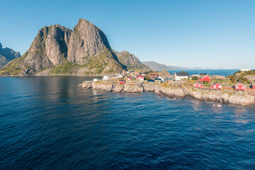 Obraz premium Colorful fisherman's wooden houses in village of Reine in Lofoten in the golden hour. Beautiful sunny afternoon in the arctic. Arctic summer in norwegian fjord. Tall rocks towering above the water.