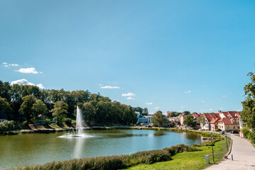 Fototapeta na wymiar Beautiful fountain in the Lake of Talsi with old buildings on the side during sunny summer day