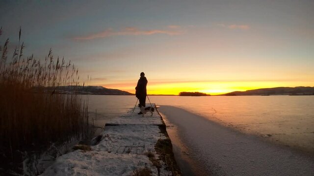 Timelapse of photographer setting up camera with tripod and taking down when finished during sunrise over Loch Leven Kinross. Photographer has a dog with him.