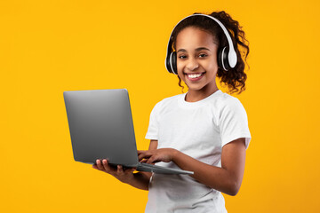 Black girl in headphones standing with laptop at studio