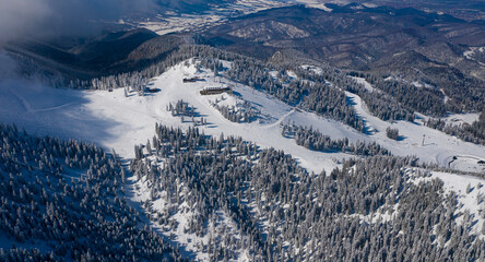 Aerial view of Poiana Brasov ski resort from Postavaru Mountains in Romania. Landmark of winter sports.