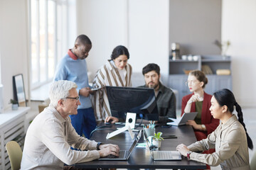 Wide angle at diverse group of business people meeting in office and using computer while...