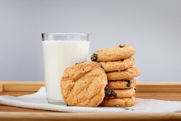 A glass of milk and cookies with raisins on a wooden tray