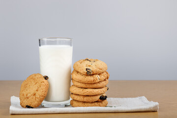 A glass of milk and cookies with raisins on the table.