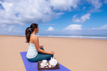 people and leisure concept- young asian woman meditating and drinking tea on the tropical beach.