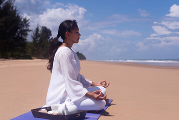 people and leisure concept- young asian woman meditating and drinking tea on the tropical beach.