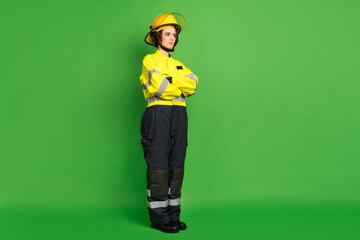 Fototapeta premium Full length photo of pretty adorable fire lady workwear yellow helmet arms folded looking empty space isolated green color background