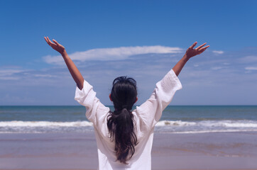 people and healthy lifestyle concept - back view of young girl enjoying tropical sea view with arms up feeling free bliss with blue sky background