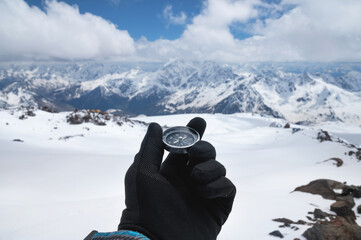 Magnetic compass in a man's hand in a black glove against the background of the snow-capped mountains of the caucasus in the afternoon. Navigation concept © yanik88