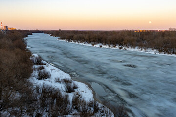 Full moon rising over forest and frozen river at sunset 