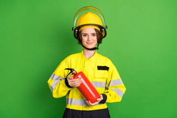 Photo of positive sweet young firewoman dressed yellow uniform helmet extinguishing smiling isolated green color background