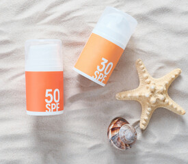 sun tan protection creme bottles on a sand next to starfish and seashell. summer skin care concept. orange and yellow pump bottles on seashore. UV protection, photoaging and skin health