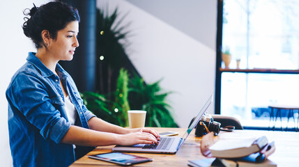 Caucasian photographer working with media files on modern laptop computer using coworking internet connection, young hipster girl browsing website via netbook application during leisure in cafe