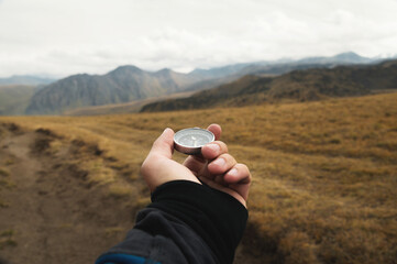 First-person view of a male traveler s hand holding a magnetic compass against the backdrop of a mountainous area. Orientation and finding your way