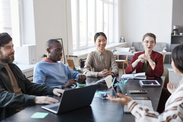 Diverse group of business people at table during briefing meeting in office, focus on smiling Asian...