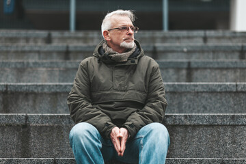 Lonely old man. A gray-haired man with wrinkles sits outside, sad. Lost a loved one, negative...