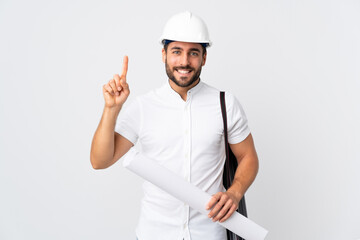 Young architect man with helmet and holding blueprints isolated on white background pointing up a...