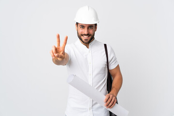 Young architect man with helmet and holding blueprints isolated on white background smiling and showing victory sign