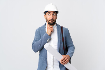Young architect man with helmet and holding blueprints isolated on white background having doubts and thinking