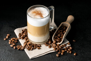 cappuccino with cinnamon in a glass cup on a black background, napkin, coffee beans, horizontal