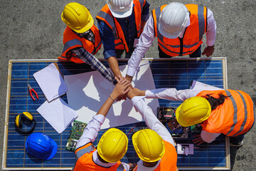 Top view of Architectural engineers putting their hands together on solar panel and his blueprints...