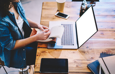 Skilled female student spending time for e learning on laptop computer with blank screen area for advertising text on knowledge website, unrecognizable woman with textbook working remotely on netbook