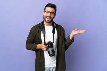 Photographer man over isolated purple background holding copyspace imaginary on the palm to insert an ad