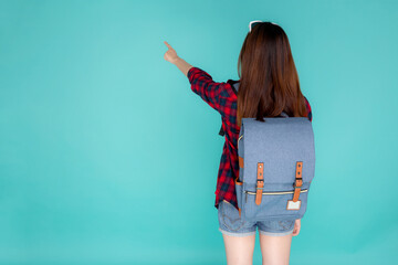 Back view of beautiful young asian woman travel with backpack pointing something isolated on blue background, rear asia girl is student or tourist in summer trip, holiday concept. - Powered by Adobe