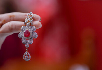 hand holding a diamond earring on red background