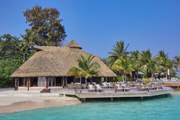 Fototapeta na wymiar Thatched Bar with Chairs in Maldives with Turquoise Sea and Blue Sky. Maldivian Resort Komandoo.