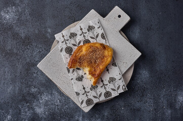 Broken piece of torrijas on craft paper on ceramic cutting board on dark background. Top view. Copy space