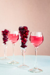 a glasses of pink gin infused with cranberry among crystal glasses of berries on light background, a row of cherry liquor or any red alcoholic cocktail, minimalism