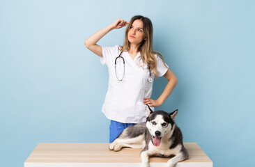 Veterinary doctor at vet clinic with Siberian Husky dog over isolated blue background having doubts and with confuse face expression