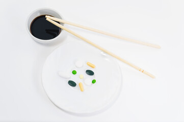 Fototapeta na wymiar Pills lie on a white plate with Chinese chopsticks isolated on a white background, selective focus. Biological active additives concept.