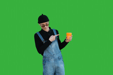 Fototapeta na wymiar Smiling young man holds an orange reusable cup in his hand and shows at it, isolated on a green background.