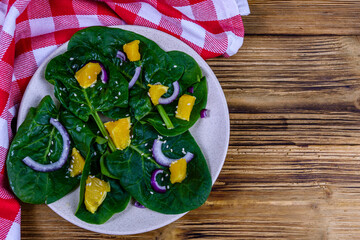 Salad with spinach leaves, pieces of orange, sesame seeds and onion in a ceramic plate. Top view