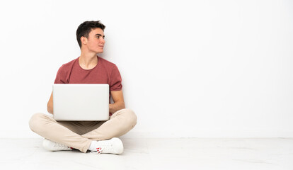 Teenager man sitting on the flor with his laptop in lateral position