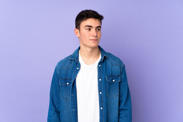 Teenager caucasian  handsome man isolated on purple background making doubts gesture looking side