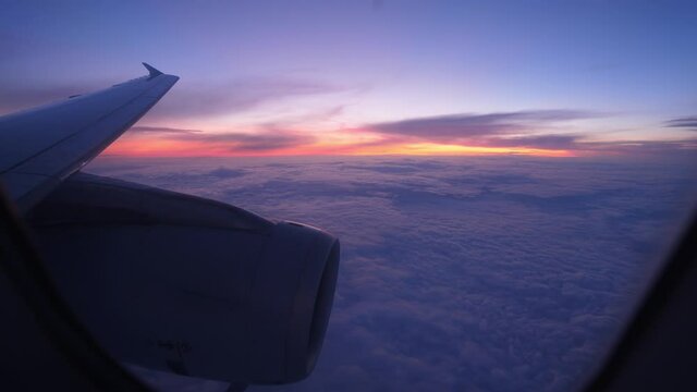 Look out from airliner window to sunset afterglow at horizon and blue clouds covering all area down. Scenic view of sky from passenger plane flying on cruise altitude at late evening hour