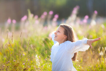 13 year old girl stands on blooming field in summer time and enjoys clean air and freedom. Child holds arms wide open like she is flying.