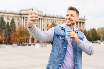 Handsome man with soda taking selfie outdoors