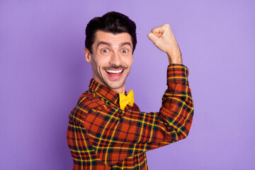 Photo of positive guy raise hand hold fist look camera wear bow tie checkered shirt isolated purple background