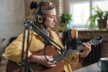 Fototapeta na wymiar Young woman in headphones playing guitar during air on the radio