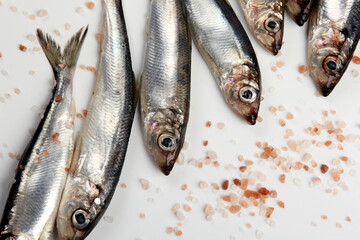 Fresh raw Baltic herring with pink Himalayan salt on a white background. Fresh small silvery fish 