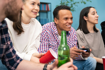 A smiling black man competes with a friend in his favorite video game. Group of friends play video games together at home, having fun