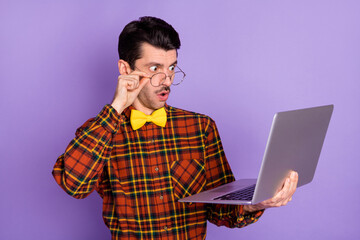 Photo of young shocked surprised amazed man in glasses see problems in project in laptop isolated on purple color background