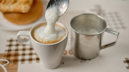 Dolewanie za pomocą łyżki spienionego mleka do kubka z kawą