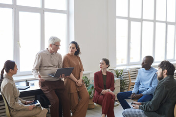 Wide angle view at contemporary diverse business team sitting in circle during strategy meeting,...